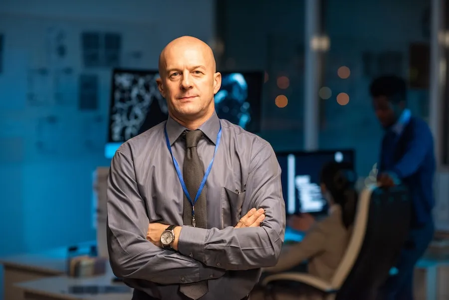 Manager standing with arms crossed in front of office workstations