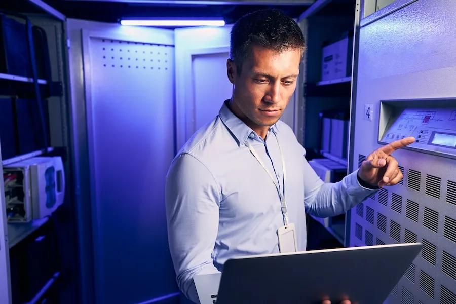 Technician with a laptop working at a control panel in a data center